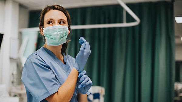 Eine Frau mit Hygiene-Maske zieht in einem Operationssaal Handschuhe an.