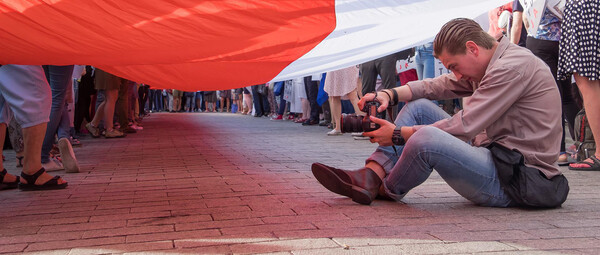 Ein Mann sitzt mit Kamera während einer Demonstration unter einer Flagge