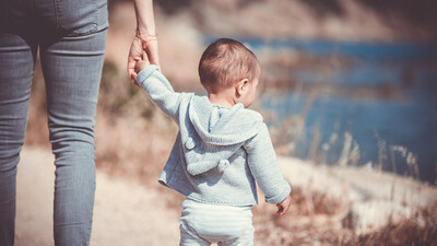 Ein gehendes Kleinkind hält die Hand der Mutter
